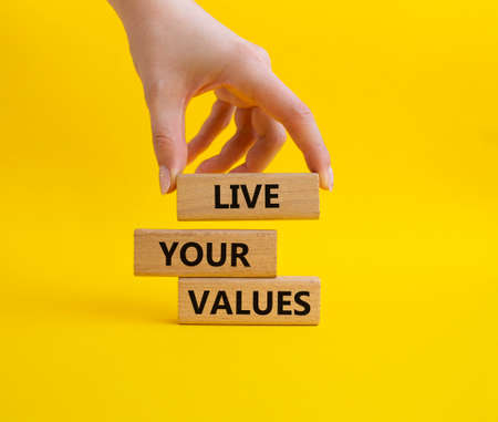 Live your values symbol. Concept words 'Live your values' on wooden blocks. Beautiful yellow background. Businessman hand. Business and Live your values concept. Copy space.の写真素材