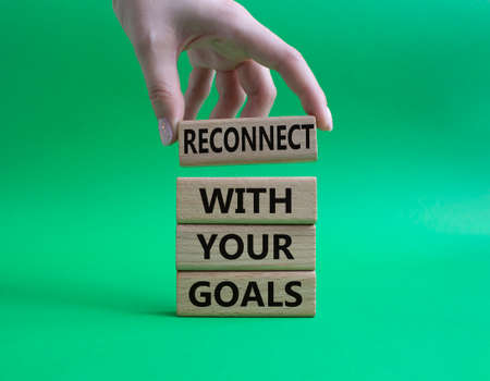 Goals symbol. Wooden blocks with words 'Reconnect with your goals'. Beautiful green background. Businessman hand. Business and 'Reconnect with your goals' concept. Copy space.の写真素材