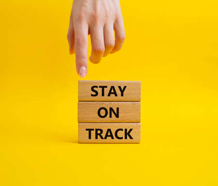 Stay on track symbol. Wooden blocks with words 'Stay on track'. Beautiful yellow background. Businessman hand. Business and 'Stay on track' concept. Copy space.の写真素材