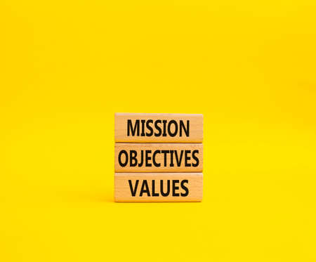 Mission Objectives Values symbol. Concept words Mission Objectives Values on wooden blocks. Beautiful yellow background. Business and Mission Objectives Values concept. Copy spaceの写真素材