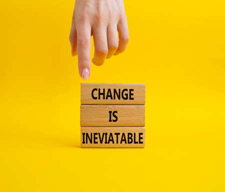 Change is Inevitable symbol. Wooden blocks with words Change is Inevitable. Beautiful yellow background. Businessman hand. Business and Change is Inevitable concept. Copy space.の写真素材