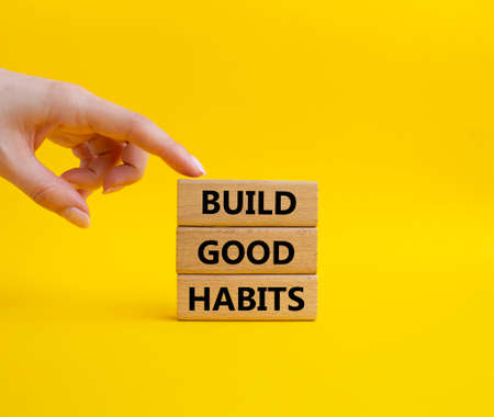 Build good habits symbol. Wooden blocks with words 'Build good habits'. Beautiful yellow background. Businessman hand. Business and 'Build good habits' concept. Copy space.の写真素材