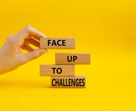 Face up to challenges symbol. Wooden blocks with words Face up to challenges. Beautiful yellow background. Businessman hand. Business and Face up to challenges concept. Copy space.の写真素材