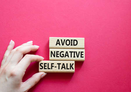 Avoid negative self-talk symbol. Concept words Avoid negative self-talk on wooden blocks. Beautiful red background. Businessman hand. Business and Avoid negative self-talk concept. Copy space.の写真素材