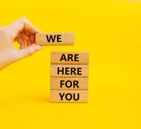 Help symbol. Wooden blocks with words 'We are here for you'. Beautiful yellow background. Businessman hand. Business and 'We are here for you' concept. Copy space.の写真素材