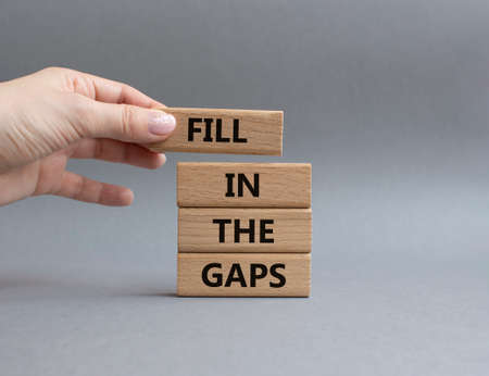 Fill in the gaps symbol. Concept words fill in the gaps on wooden blocks. Beautiful grey background. Businessman hand. Business and fill in the gaps concept. Copy space.の写真素材