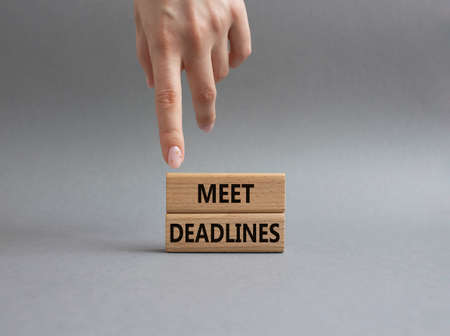 Meet Deadlines symbol. Concept word Meet Deadlines on wooden blocks. Beautiful grey background. Businessman hand. Business and Meet Deadlines concept. Copy spaceの写真素材