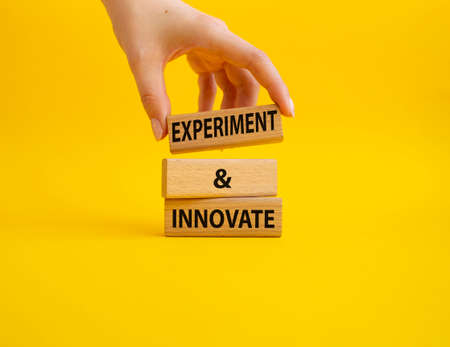 Experiment and innovate symbol. Concept words Experiment and innovate on wooden blocks. Beautiful yellow background. Businessman hand. Business and Experiment and innovate concept. Copy space.の写真素材