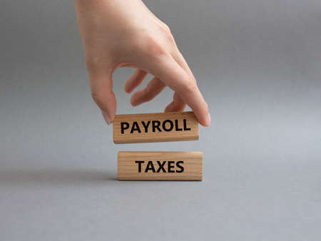 Payroll taxes symbol. Concept word Payroll taxes on wooden blocks. Beautiful grey background. Businessman hand. Business and Payroll taxes concept. Copy spaceの写真素材