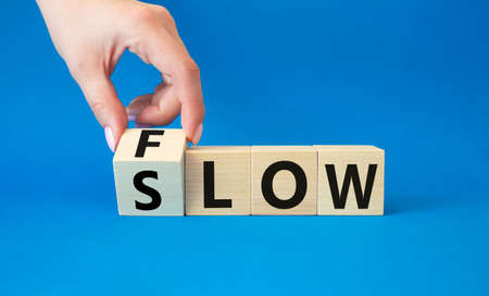 Flow and Slow symbol. Concept words Flow and Slow on wooden cubes. Beautiful blue background. Businessman hand. Business and Flow and Slow concept. Copy space.の写真素材