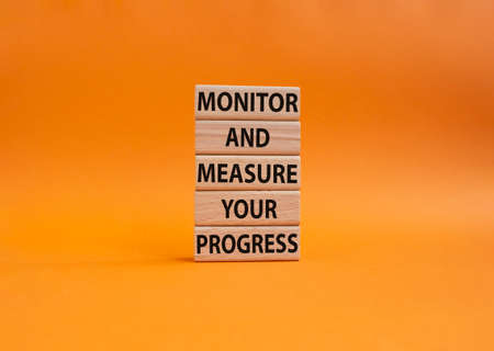 Monitor and Measure your Progress symbol. Wooden blocks with words Monitor and Measure your Progress. Beautiful orange background. Business and Monitor and Measure your Progress Copy spaceの写真素材
