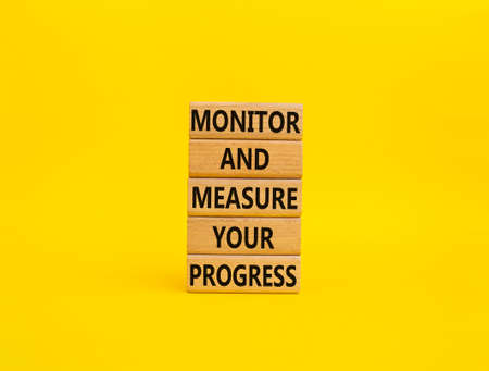 Monitor and Measure your Progress symbol. Wooden blocks with words Monitor and Measure your Progress. Beautiful yellow background. Business and Monitor and Measure your Progress Copy spaceの写真素材