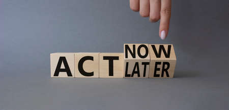 Act Now vs Act Later symbol. Businessman hand points at cubes with words Act Now vs Act Later. Beautiful gray background. business concept. copy spaceの写真素材