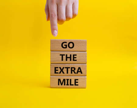 Go the extra mile symbol. Wooden blocks with words Go the extra mile. beautiful yellow background. businessman hand. Business and Go the extra mile concept. copyspace.の写真素材