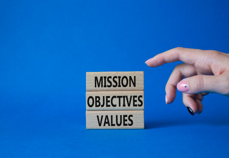 Mission Objectives Values symbol. Concept words Mission Objectives Values on wooden blocks. beautiful blue background. businessman hand. Business and Mission Objectives Values concept. copy spaceの写真素材