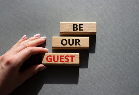 Be our guest symbol. Concept word Be our guest on wooden blocks. Beautiful gray background. businessman hand. Business and Be our guest concept. copy spaceの写真素材