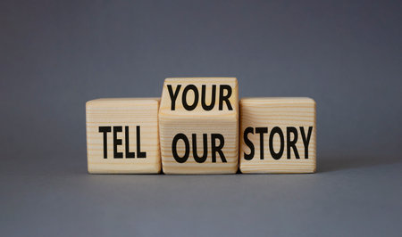 Tell Your or Our story symbol. Turned wooden cubes with words Tell your story to Tell our story. Beautiful grey background. Business concept. Copy spaceの写真素材