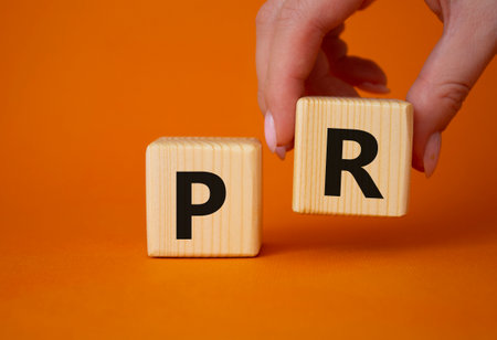 PR-public relations symbol. Concept word PR on wooden cubes. businessman hand. Beautiful orange background. Business and PR concept. copyspace.の写真素材