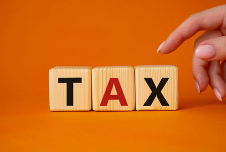 tax symbol. Wooden cubes with word tax. businessman hand. Beautiful orange background. Business and finance and tax concept. copyspace.の写真素材