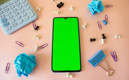 Top view, Smart phone on pink background with green screen and office supplies, Close-up the cell...