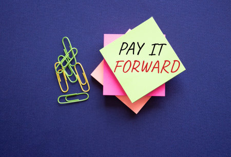Pay it forward symbol. Concept words Pay it forward on yellow steaky note with paper clips. beautiful pink background. Business and Pay it forward concept. copyspace.の写真素材