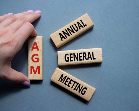 AGM - Annual general meeting symbol. Concept word AGM on wooden blocks. Businessman hand. Beautiful gray background. Business and AGM concept. Copy space.の写真素材