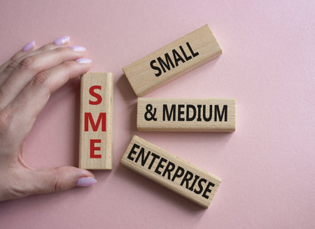 SME - Small and Medium Enterprise symbol. Wooden cubes with words SME. Businessman hand. Beautiful pink background. Business and SME concept. Copy space.の写真素材