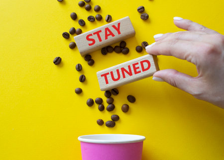 Stay Tuned symbol. Concept word Stay Tuned on wooden blocks. Businessman hand. Beautiful yellow background with coffee cup. Business and Stay Tuned concept. Copy spaceの写真素材