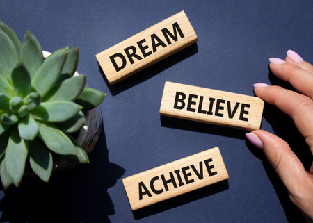 Dream Believe Achieve symbol. Wooden blocks with words Dream Believe Achieve. Businessman hand. Beautiful deep blue background with succulent plant. Business and Dream Believe Achieve concept. Copy space.の写真素材