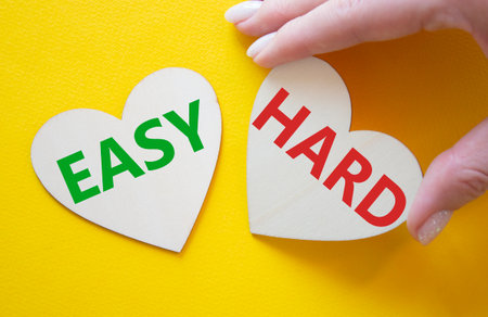 Easy or Hard symbol. Concept word Easy or Hard on wooden hearts. Businessman hand. Beautiful yellow background. Business and Easy or Hard concept. Copy spaceの写真素材