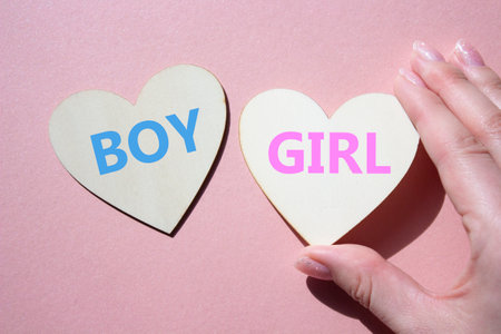 Boy or Girl symbol. Concept word Boy or Girl on wooden hearts. Man hand. Beautiful pink background. Gender and Boy or Girl concept. Copy spaceの写真素材