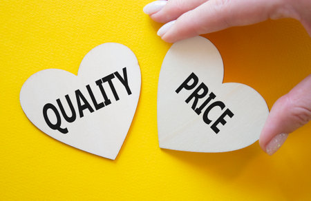 Price or Quality symbol. Concept word Price or Quality on wooden hearts. Businessman hand. Beautiful yellow background. Business and Price or Quality concept. Copy spaceの写真素材