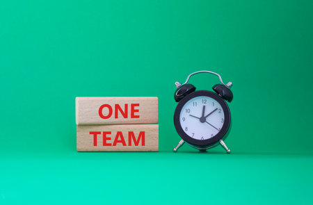 One Team symbol. Concept word One Team on wooden blocks. Beautiful green background with alarm clock. Business and One Team concept. Copy spaceの写真素材