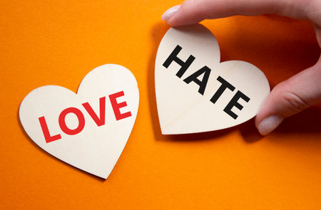 Love vs Hate symbol. Concept word Love vs Hate on wooden hearts. Businessman hand. Beautiful orange background. Business and Love vs Hate concept. Copy spaceの写真素材