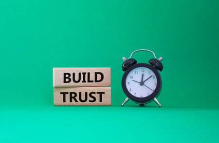 Build trust symbol. Wooden blocks with words Build trust. Beautiful green background with alarm clock. Business and Build trust concept. Copy space.の写真素材