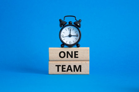 One Team symbol. Concept word One Team on wooden blocks. Beautiful blue background with alarm clock. Business and One Team concept. Copy spaceの写真素材