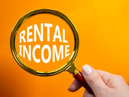 Rental Income symbol. Magnifying glass with words Rental Income. Beautiful orange background. Businessman hand. Business and Rental Income concept. Copy space.の写真素材
