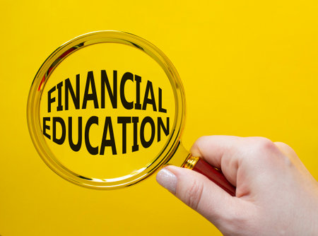 Financial Education symbol. Magnifying Glass with Concept word Financial Education. Businessman hand. Beautiful yellow background. Business and Financial Education concept. Copy spaceの写真素材