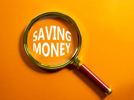 Saving Money symbol. Concept words Saving Money on magnifying glass. Beautiful orange background. Business and Saving Money concept. Copy space.の写真素材