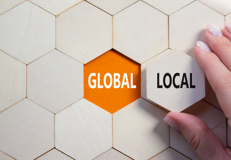 Global and Local symbol. Concept word Global and Local on wooden comb puzzle. Businessman hand. Beautiful orange background. Business and Global and Local concept. Copy spaceの写真素材