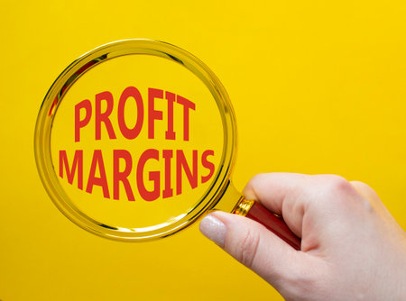 Profit Margins symbol. Magnifying glass with words Profit Margins. Beautiful yellow background. Businessman hand. Business and Profit Margins concept. Copy space.の写真素材