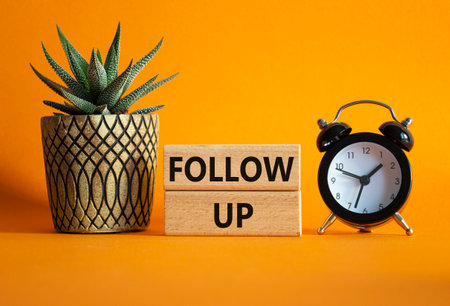 Follow up symbol. Concept word Follow up on wooden blocks. Beautiful orange background with alarm clock and succulent plant. Business and Follow up concept. Copy spaceの写真素材