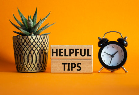 Helpful tips symbol. Wooden blocks with words Helpful tips. Beautiful orange background with alarm clock and succulent plant. Business and Helpful tips concept. Copy space.の写真素材