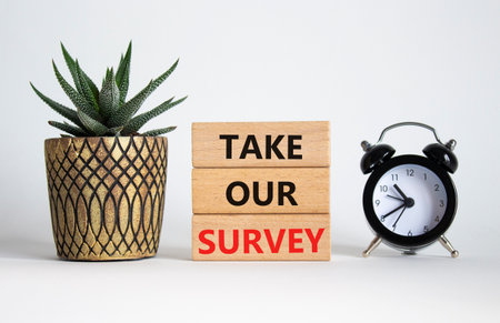 Take our Survey now symbol. Wooden blocks with words Take our Survey. Beautiful white background with succulent plant and alarm clock. Business and Take our Survey concept. Copy space.の写真素材