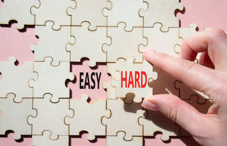 Easy or Hard symbol. Concept word Easy or Hard on wooden puzzle. Businessman hand. Beautiful pink background. Business and Easy or Hard concept. Copy spaceの写真素材
