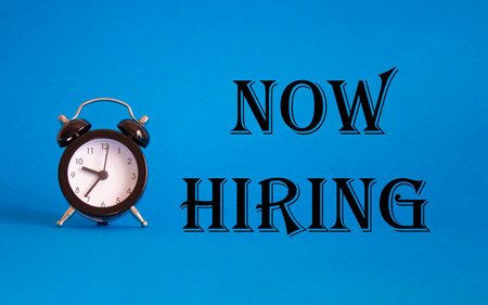 Now Hiring symbol. Concept word Now Hiring on Beautiful blue background with alarm clock. Business and Now Hiring concept. Copy spaceの写真素材