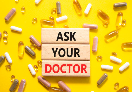 Ask Your Doctor symbol. Concept word Ask Your Doctor on wooden blocks. Beautiful yellow background with pills. Medicine and Ask Your Doctor concept. Copy spaceの写真素材