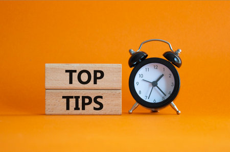 Top Tips symbol. Concept words Top Tips on wooden blocks. Beautiful orange background with alarm clock. Business and Top Tips concept. Copy space.の写真素材