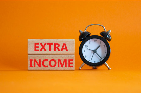 Extra Income symbol. Concept words Extra Income on wooden blocks. Beautiful orange background with alarm clock. Business and Extra Income concept. Copy space.の写真素材