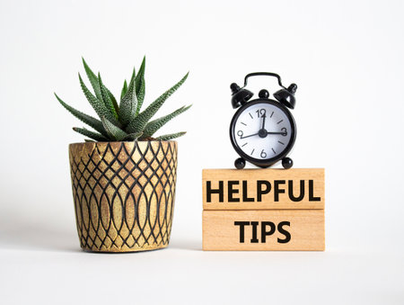 Helpful tips symbol. Wooden blocks with words Helpful tips. Beautiful white background with alarm clock and succulent plant. Business and Helpful tips concept. Copy space.の写真素材